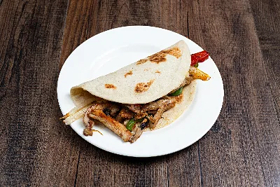 A folded flour tortilla taco filled with sliced chicken fajita and grilled bell peppers.