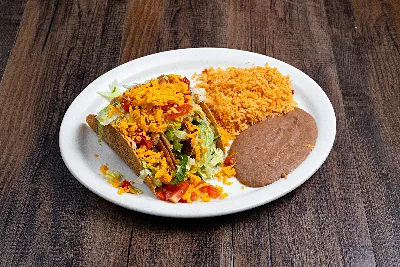 Three crisp corn tacos filled with lettuce, tomato and shredded cheddar, with Mexican rice and refried beans on a white oval plate.