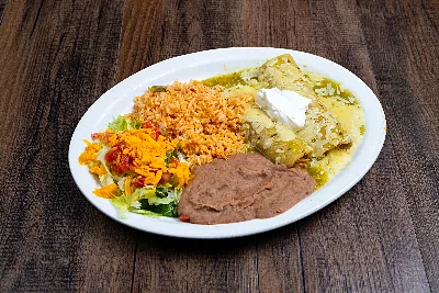 Two chicken enchiladas under green tomatillo sauce topped with sour cream, beside Mexican rice, refried beans and salad.
